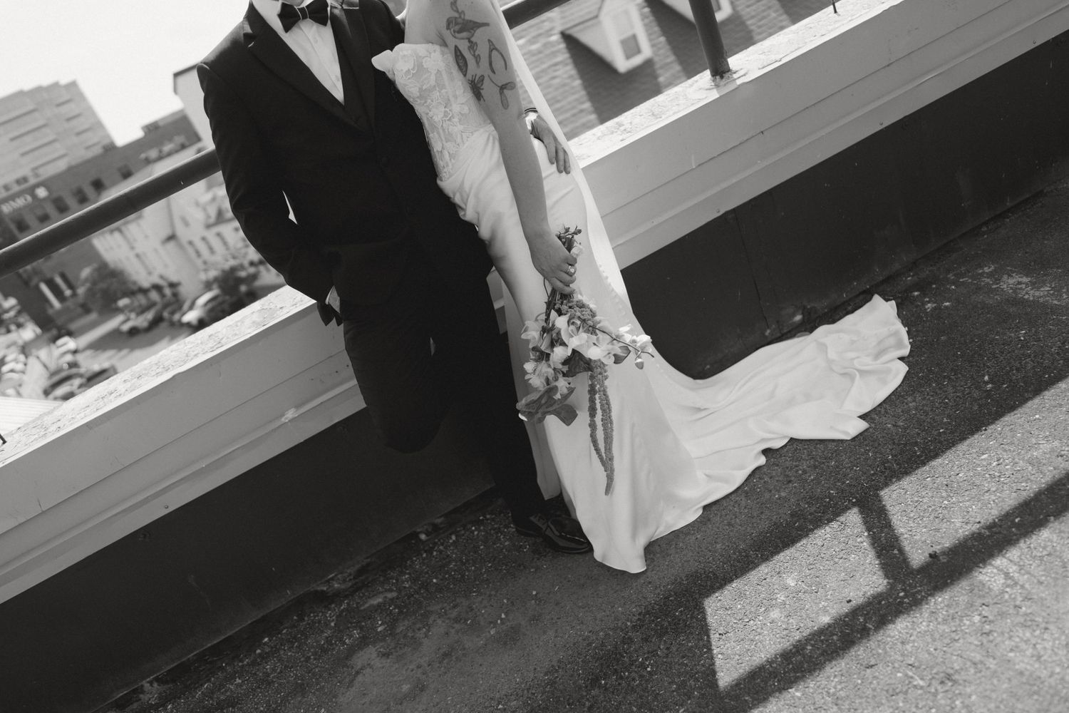 Black and white photo of a bride and groom standing together on a rooftop, bride holding a bouquet.