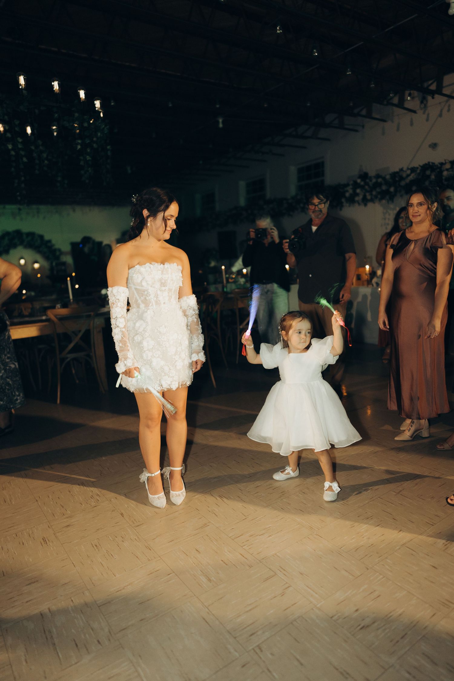 Wedding party dances on a wooden dance floor during a reception celebration with string lights overhead.