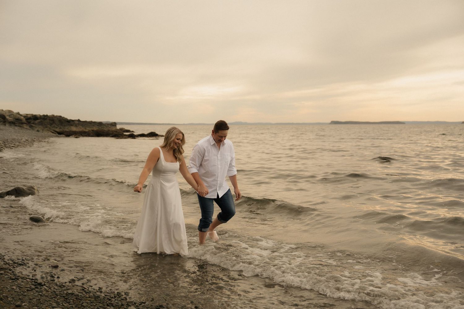 Romantic beach photoshoot with couple playing in shallow ocean waters during sunset.