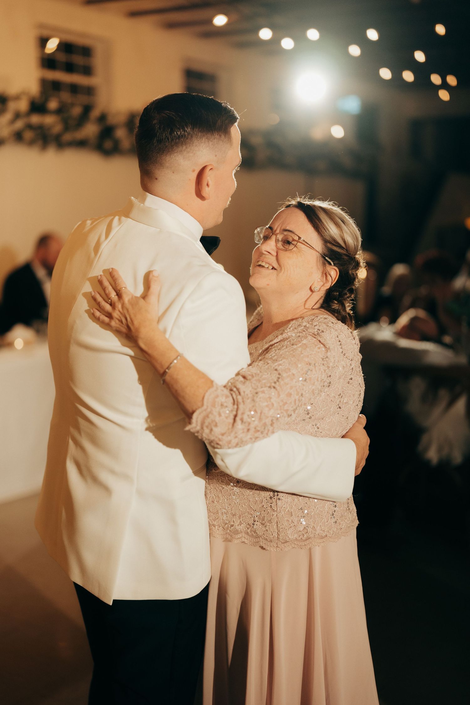 A tender moment captured during a wedding dance as two people embrace on the dance floor in warm lighting.
