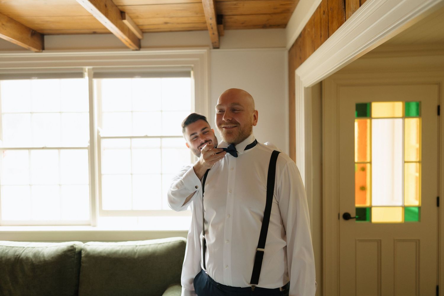 People in formal attire dancing in a bright room with wooden beams and white walls.
