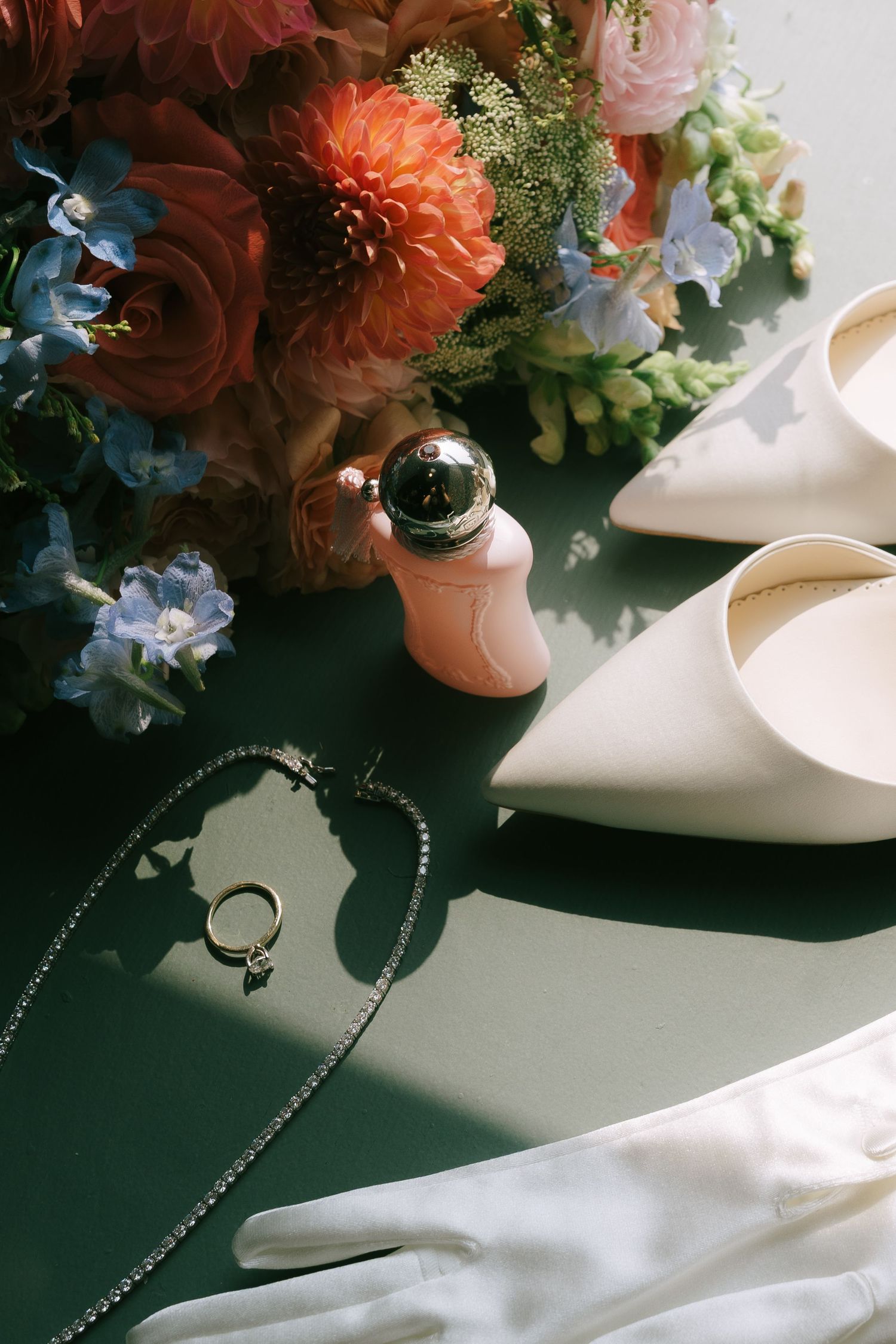 Wedding details including bridal shoes, floral arrangements, and jewelry on a white surface.