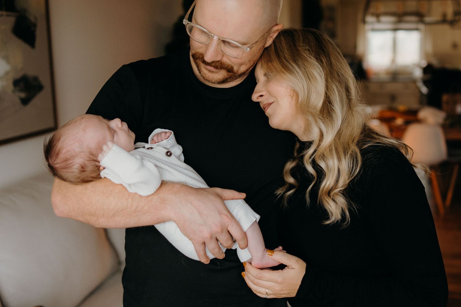 Loving parents cradle their newborn baby in a warmly lit home setting.