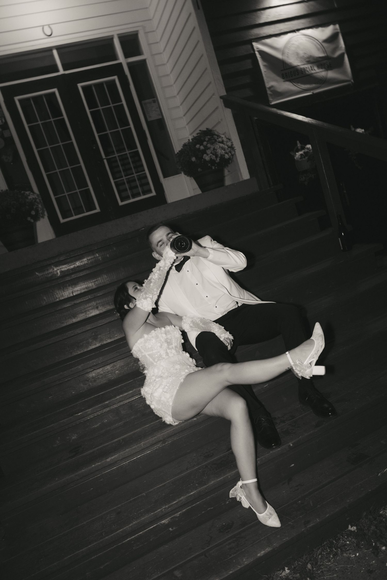 A person in a white dress lies dramatically on a dark wooden floor in a black and white photograph.