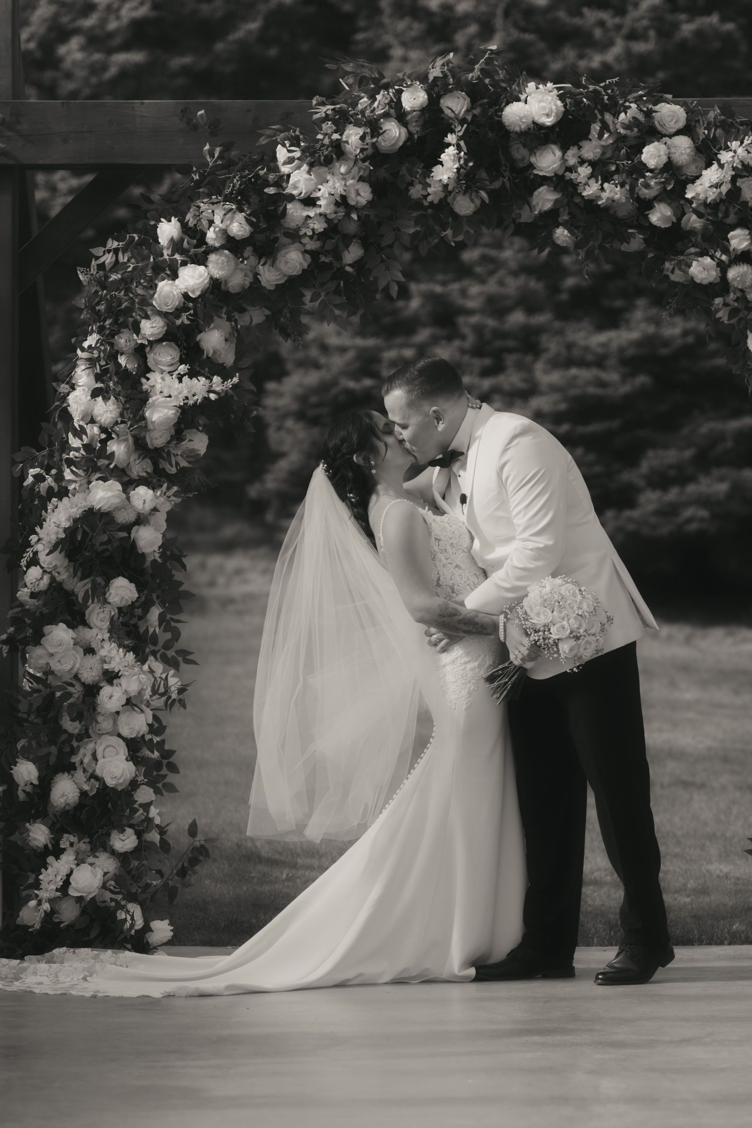 A black and white wedding ceremony series showing a couple getting married under a floral arch in an outdoor setting.