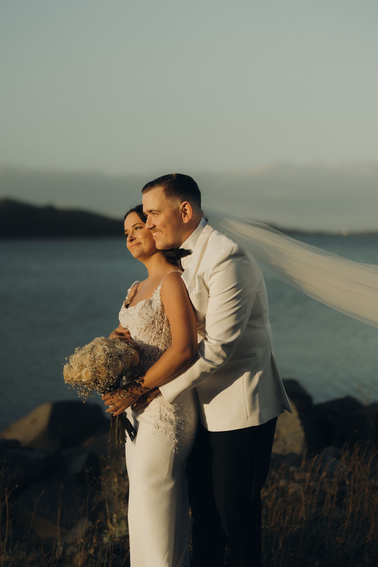 Romantic wedding couple embraces against scenic mountain backdrop during golden hour sunset.