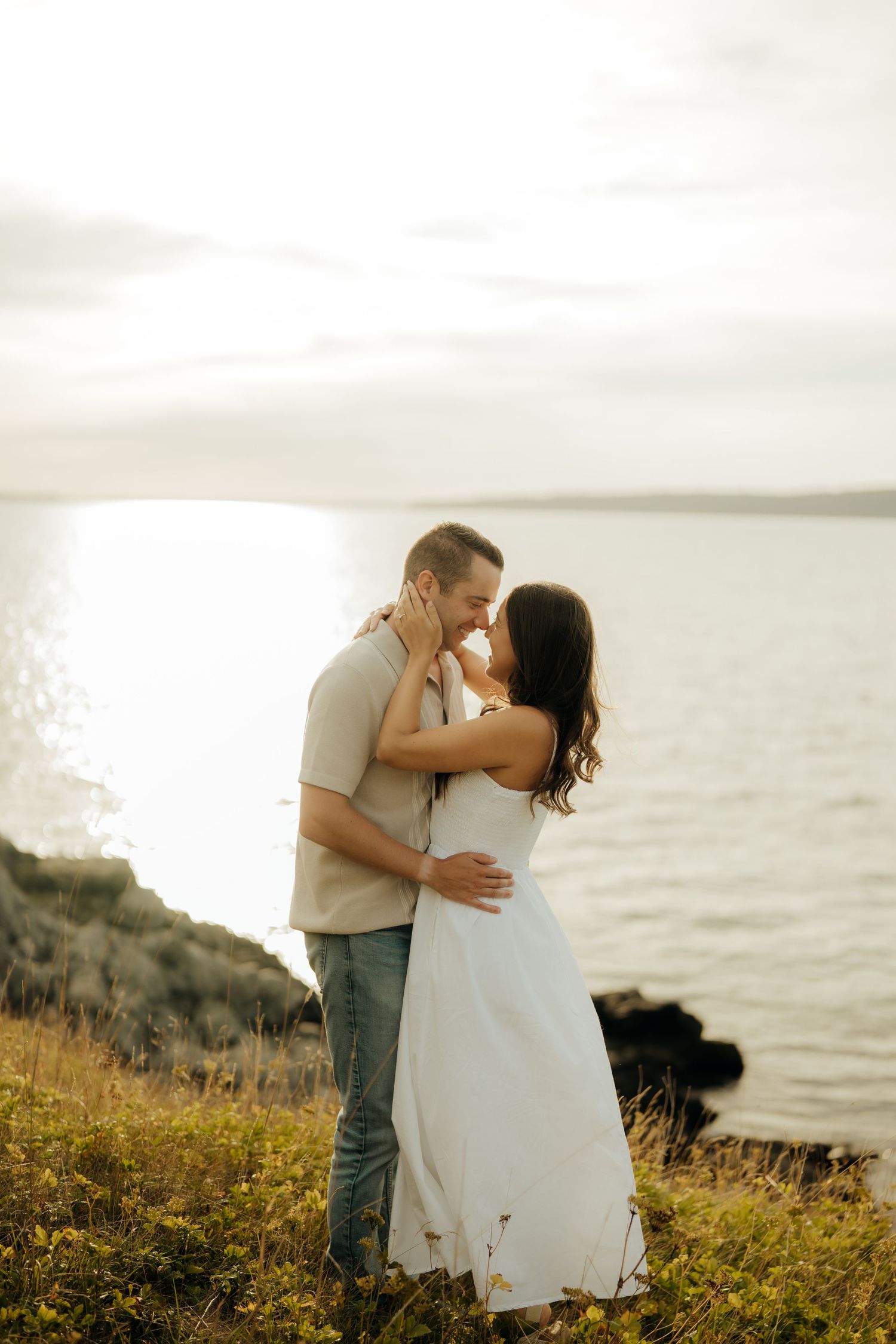 A romantic couple shares tender moments at sunset along a coastal cliff dotted with yellow wildflowers.