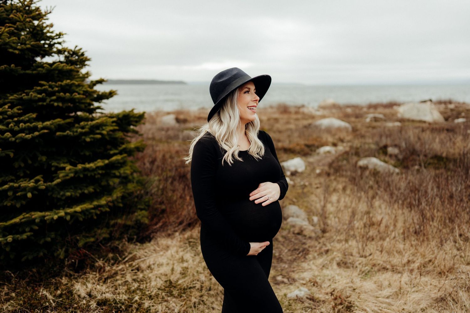 A couple shares tender moments along a rugged coastline wearing dark clothing.