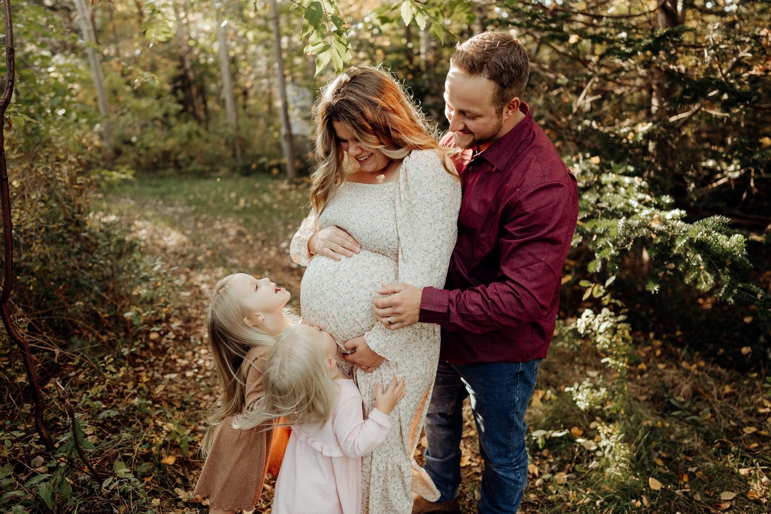 An intimate family photoshoot in a wooded setting with soft natural lighting.