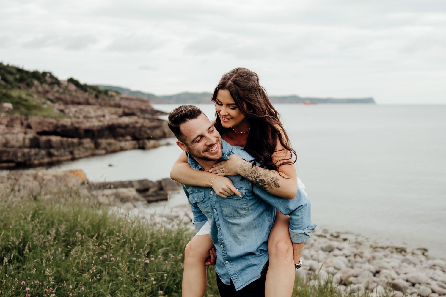 A playful couple enjoys a casual photoshoot along a scenic coastal hiking trail.