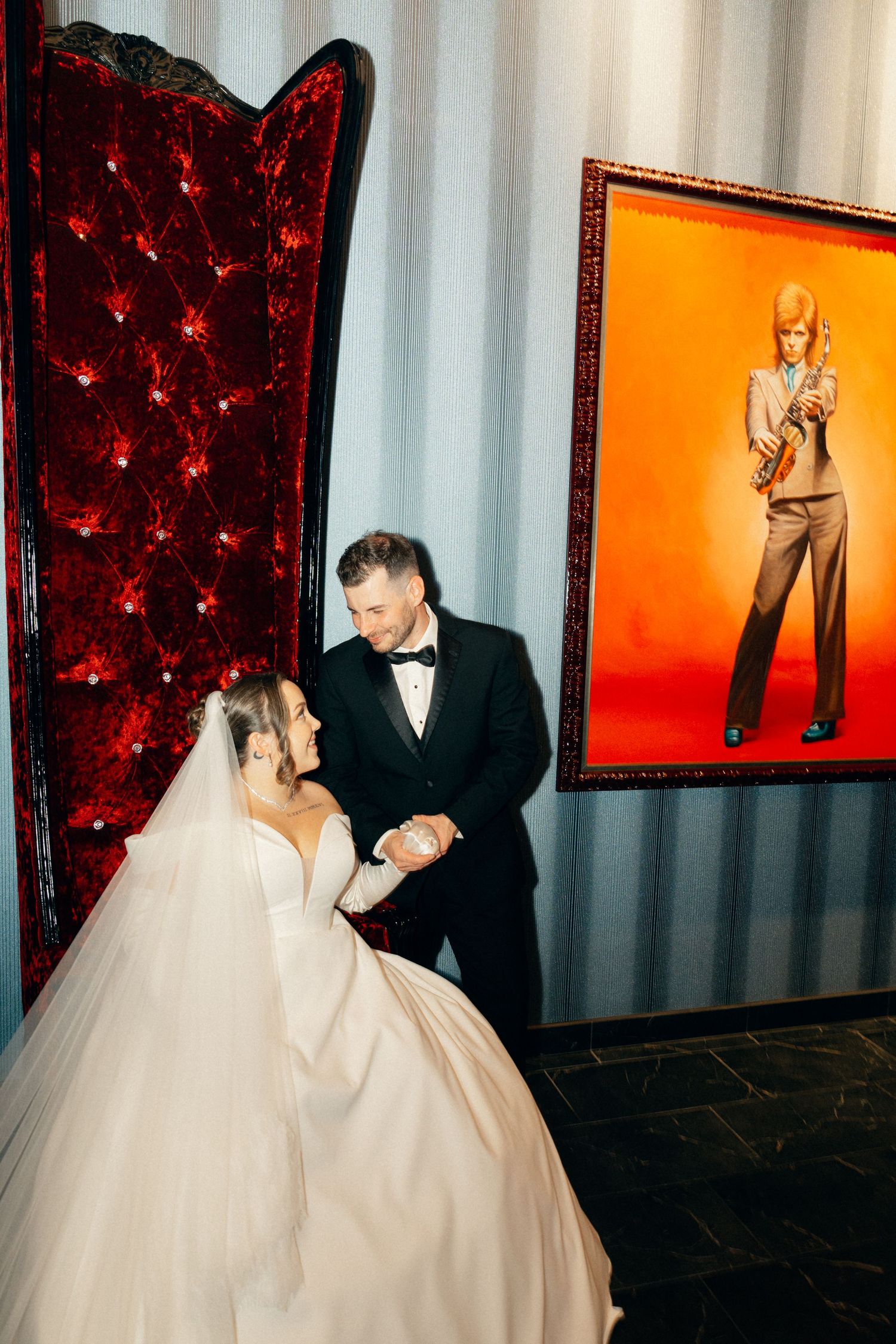 Wedding photo series with red tufted chairs and orange wall art creating dramatic backdrop.