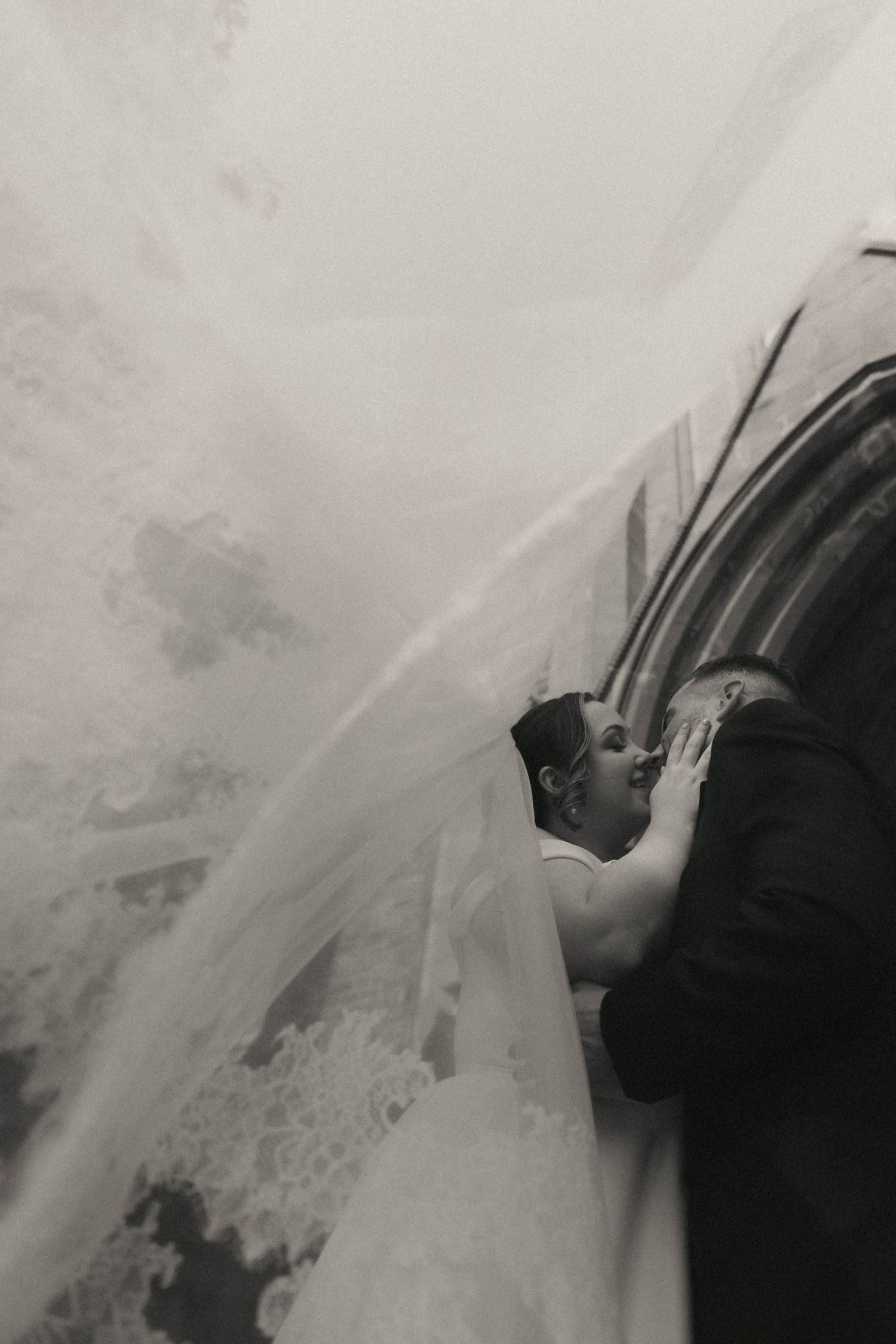 Artistic black and white wedding portrait with dramatic veil movement.