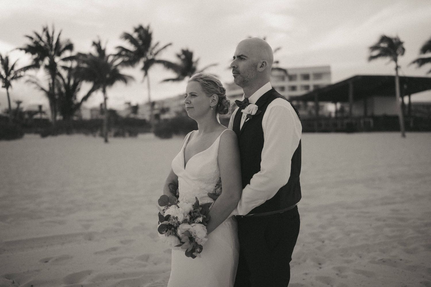 Wedding couple walking along palm-lined beach at sunset.