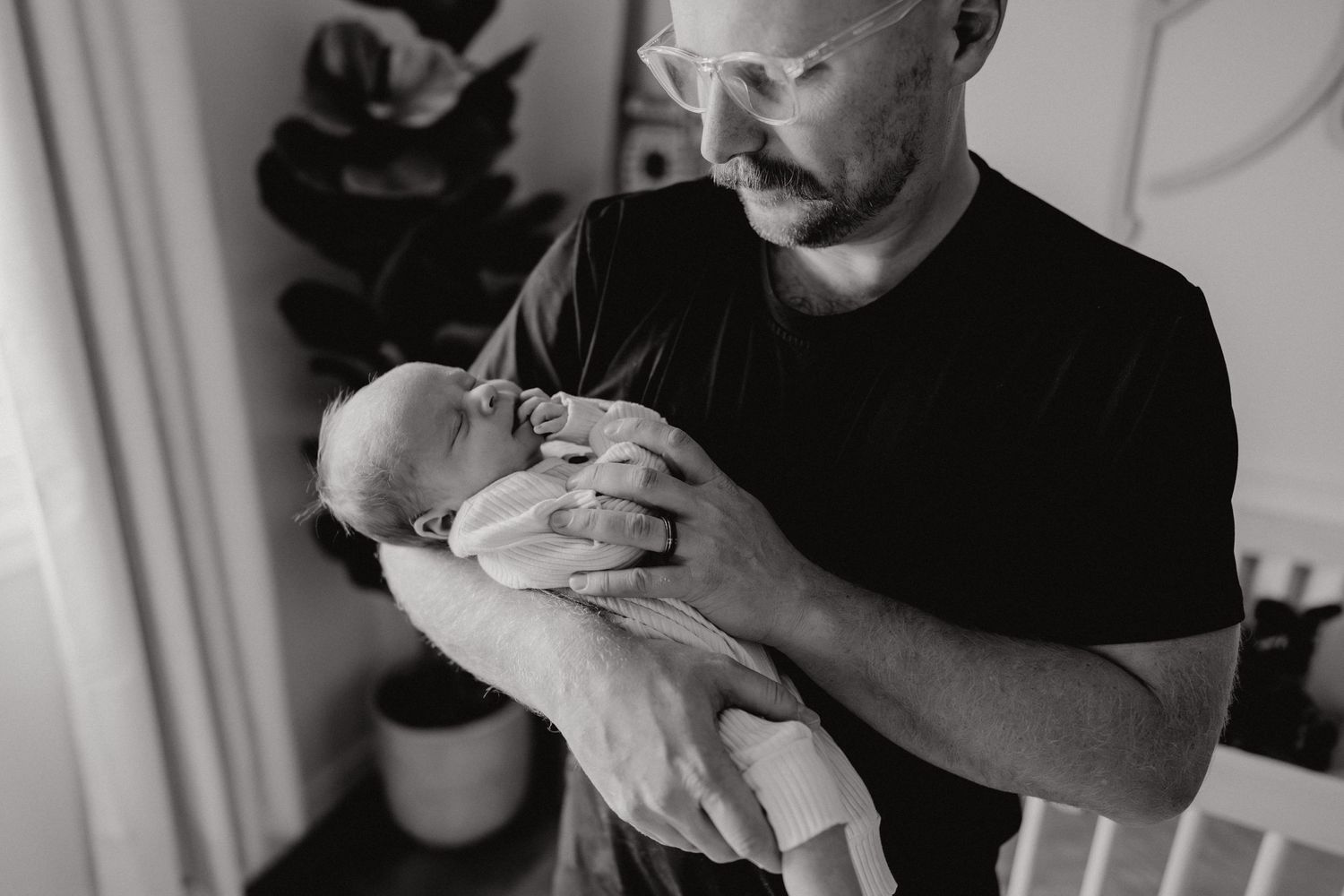 Parent holding and smiling at a tiny baby in a brightly lit nursery room.