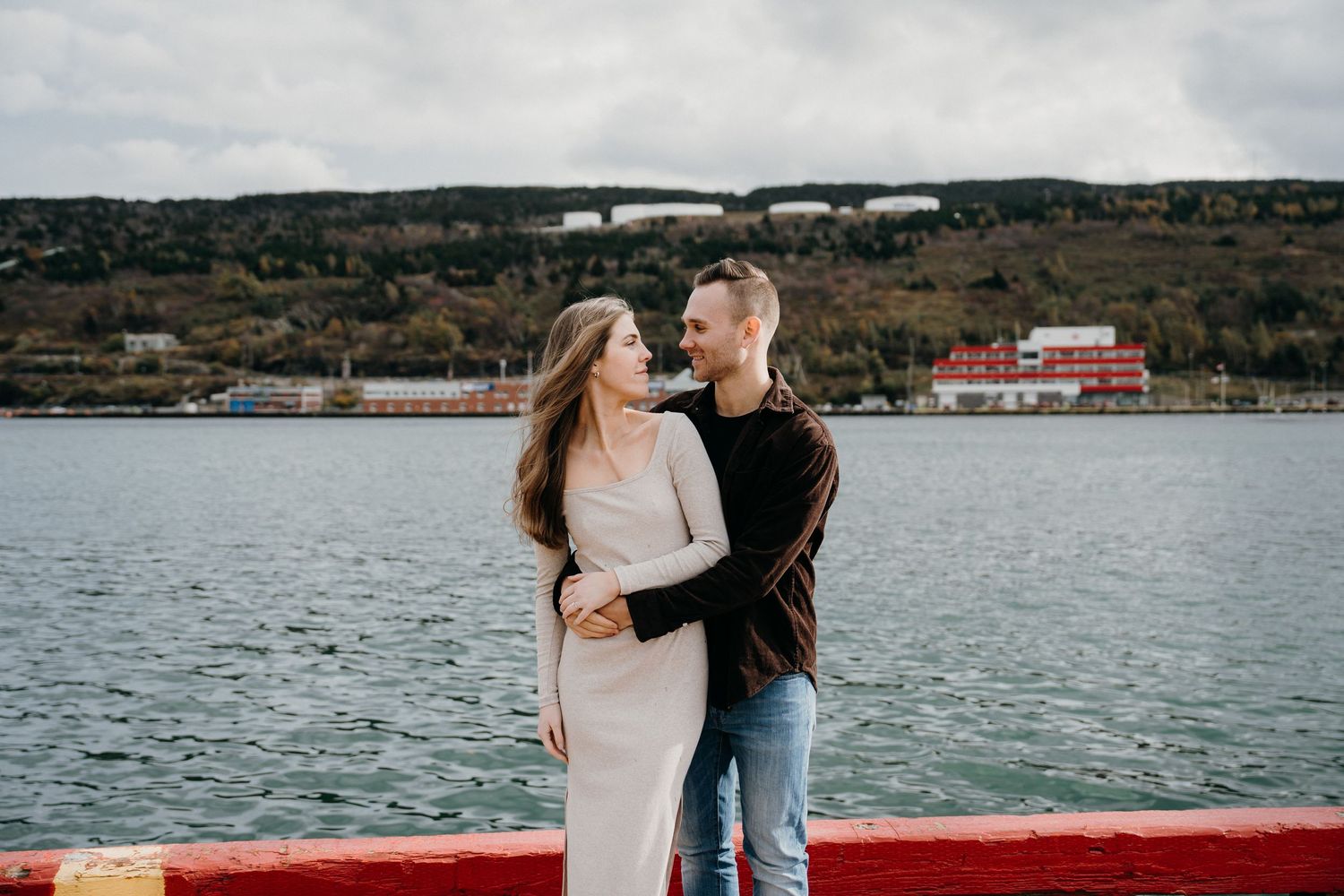 A tender moment photographed by the water with mountains and harbor buildings visible in the distance.
