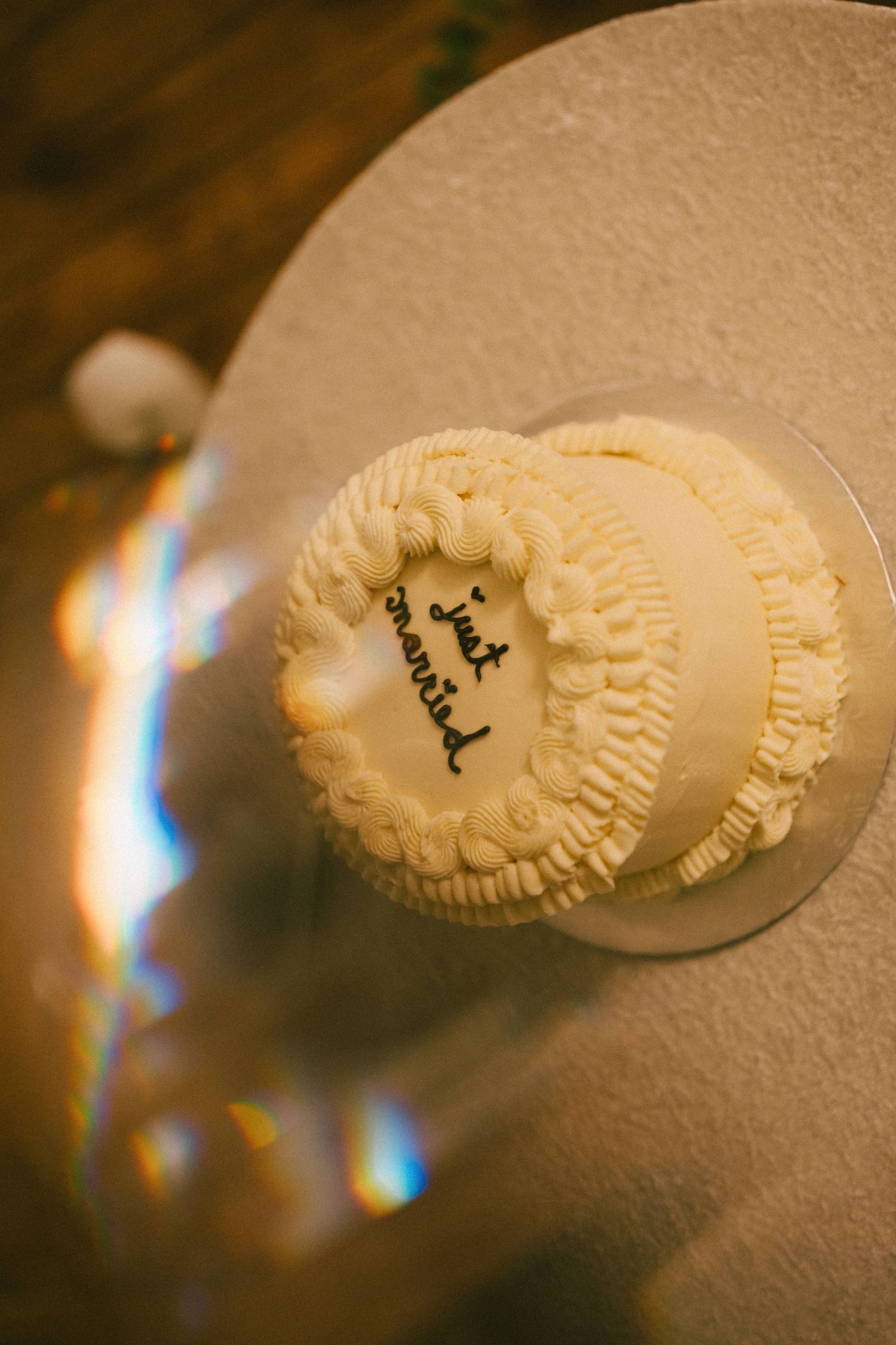 Small white wedding cake with “just married” inscription, decorated with piped buttercream rosettes, on a round silver stand.