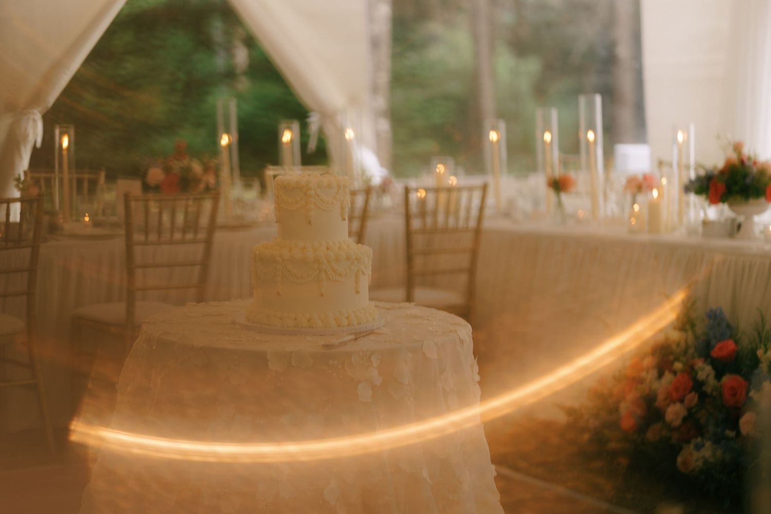 A softly lit wedding reception tent with glowing uplighting along white draped fabric walls.