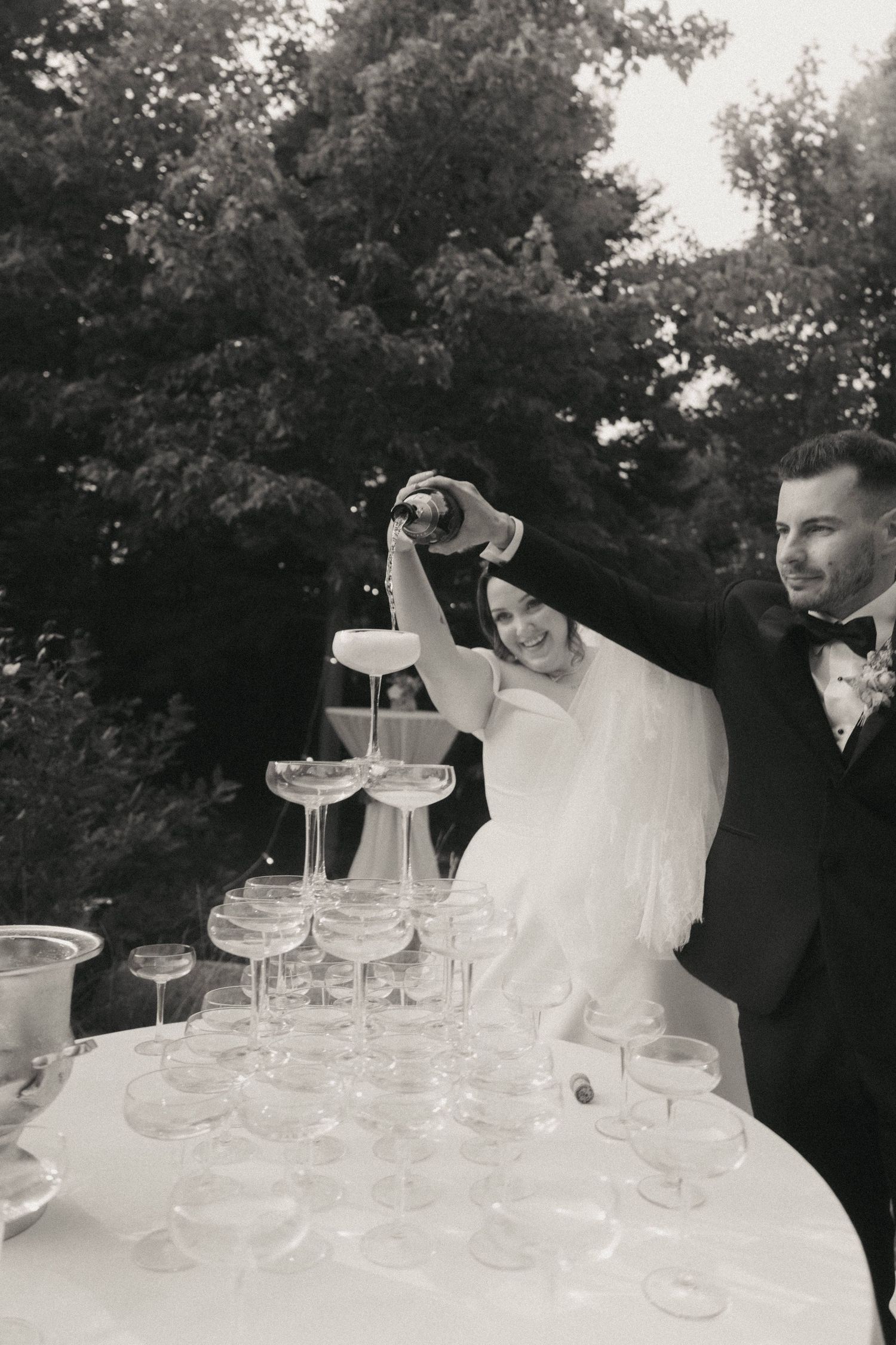 Champagne tower being assembled with coupe glasses at an outdoor celebration.