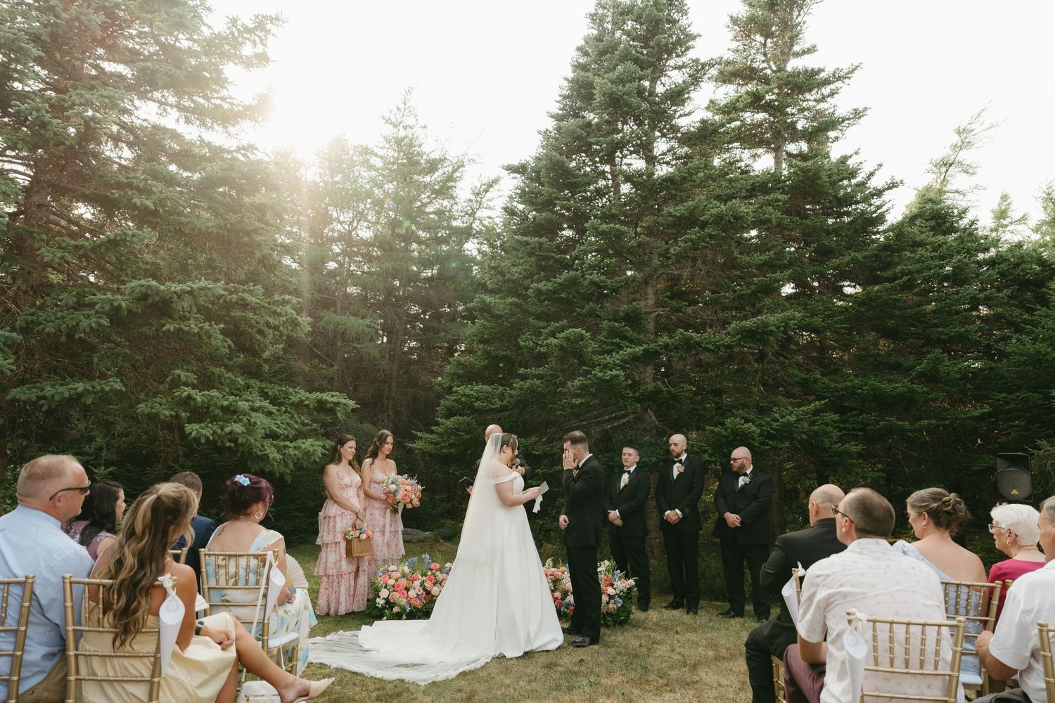 Sunlit outdoor wedding ceremony with evergreen trees creating a natural backdrop.