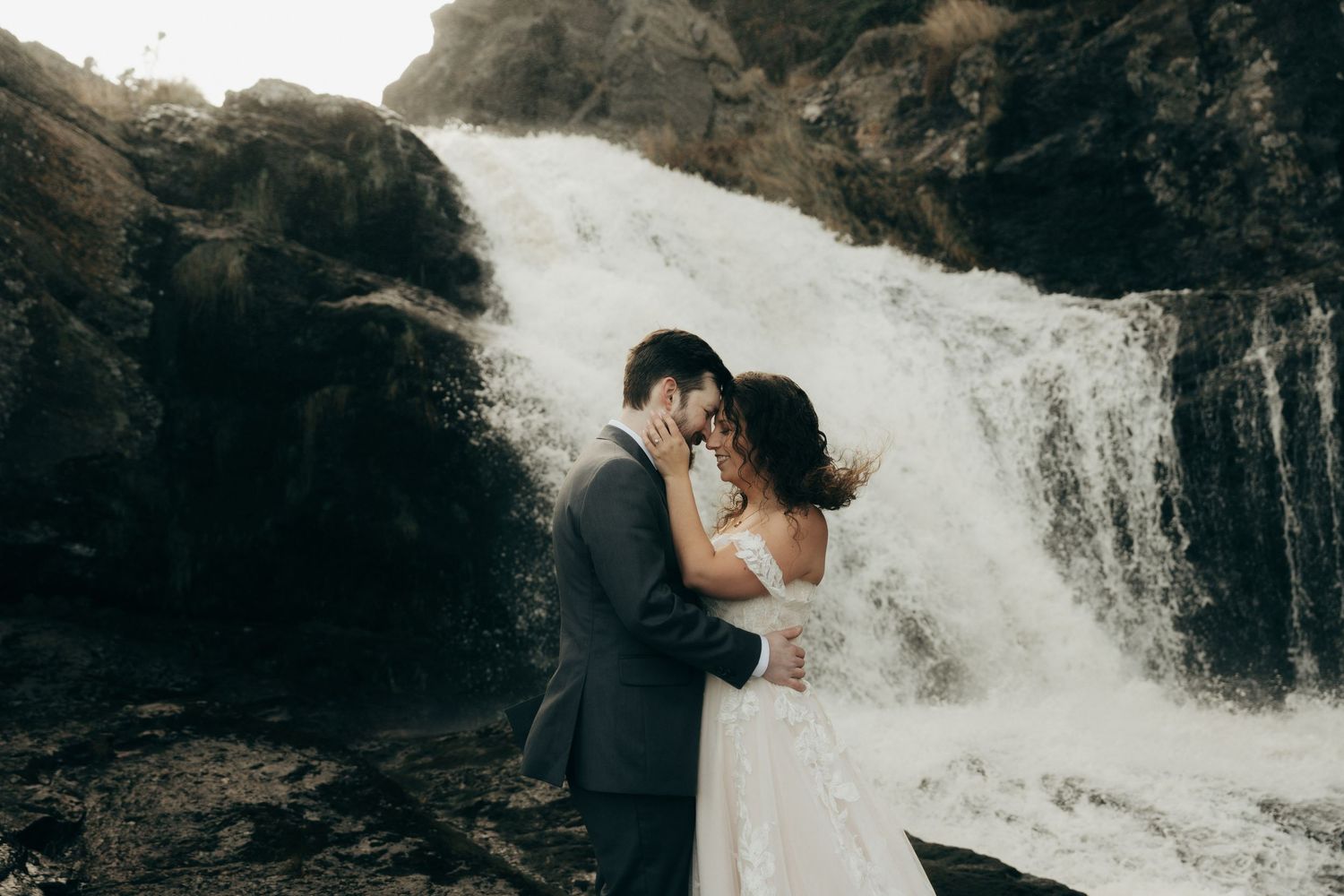 Two figures embrace near a cascading waterfall in a dramatic wedding photo shoot.