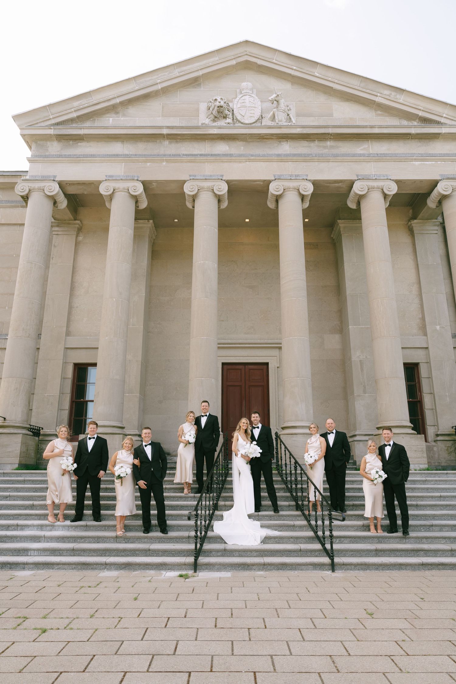 Wedding ceremony group posed on steps of neoclassical building with columned facade.