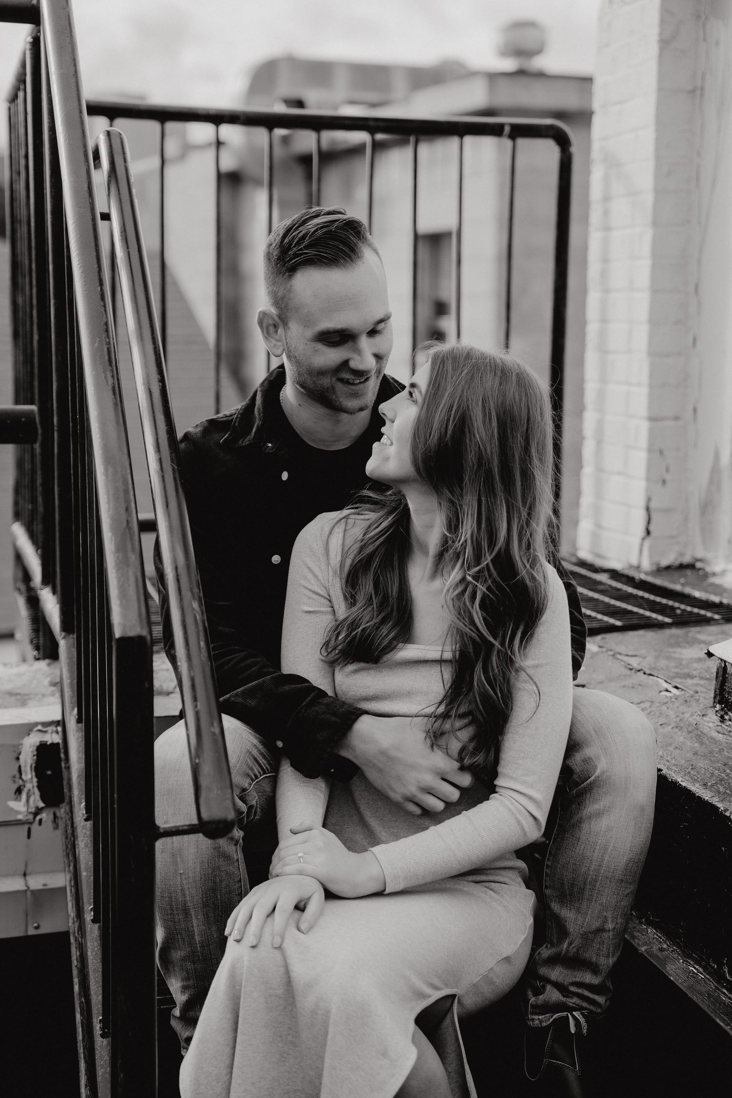 Black and white photos of couple embracing on urban rooftop setting.