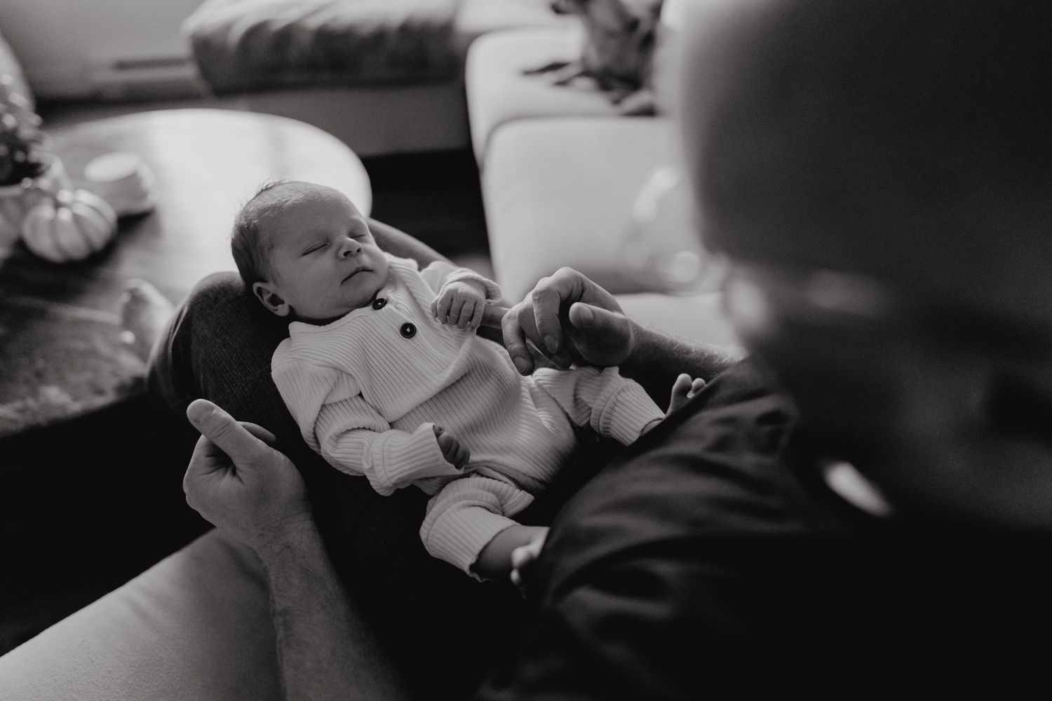 Moody black and white photograph of baby resting in gentle embrace.