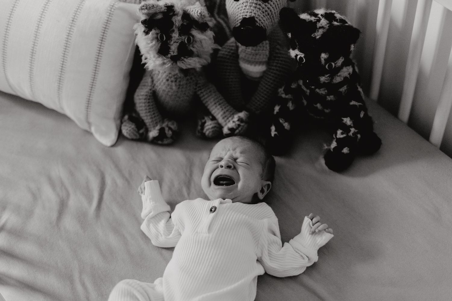 Overhead view of infant resting in crib with toys along the side.