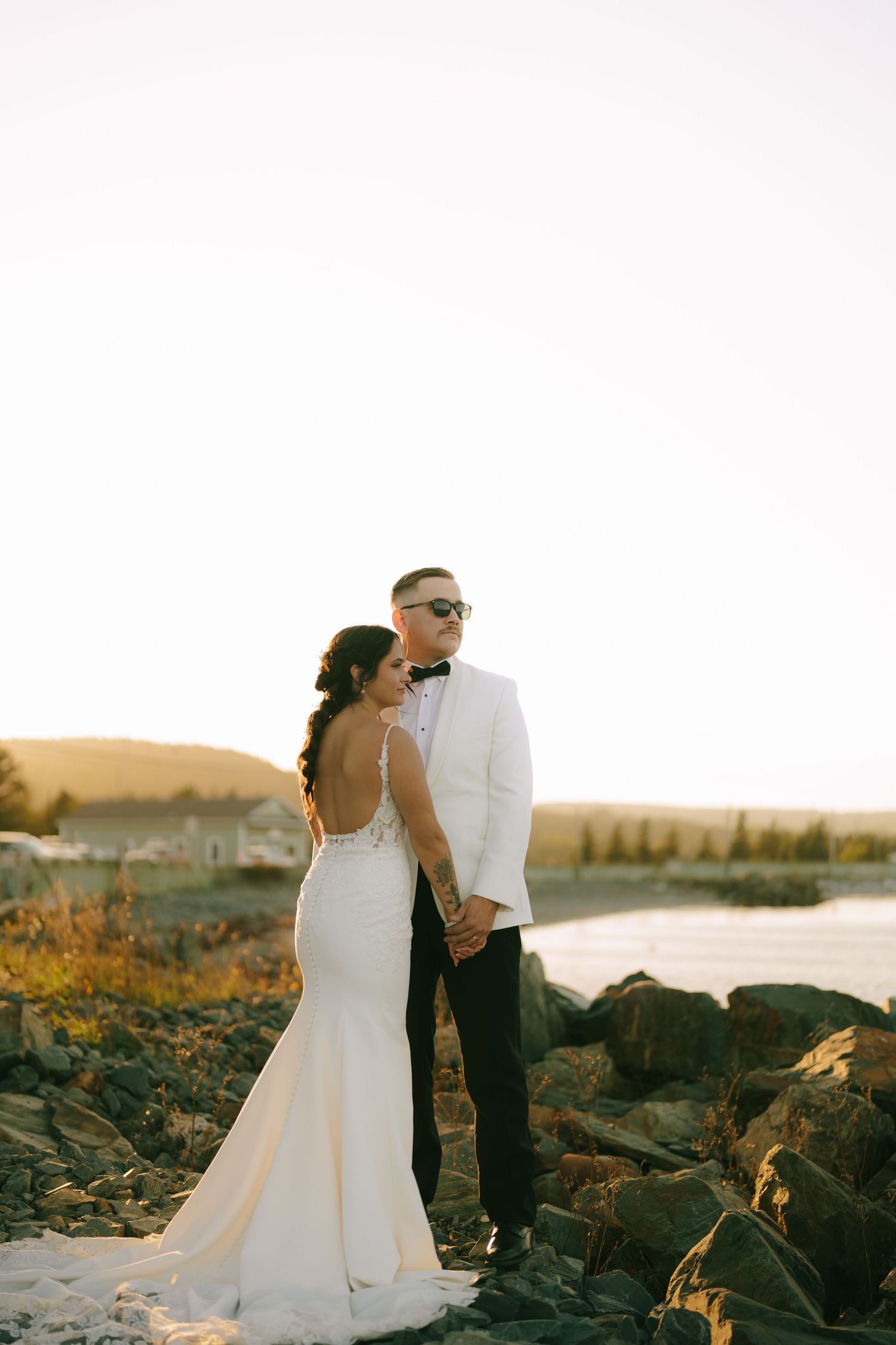 A romantic sunset beach wedding photoshoot with a couple standing among coastal rocks as golden light illuminates the scene.