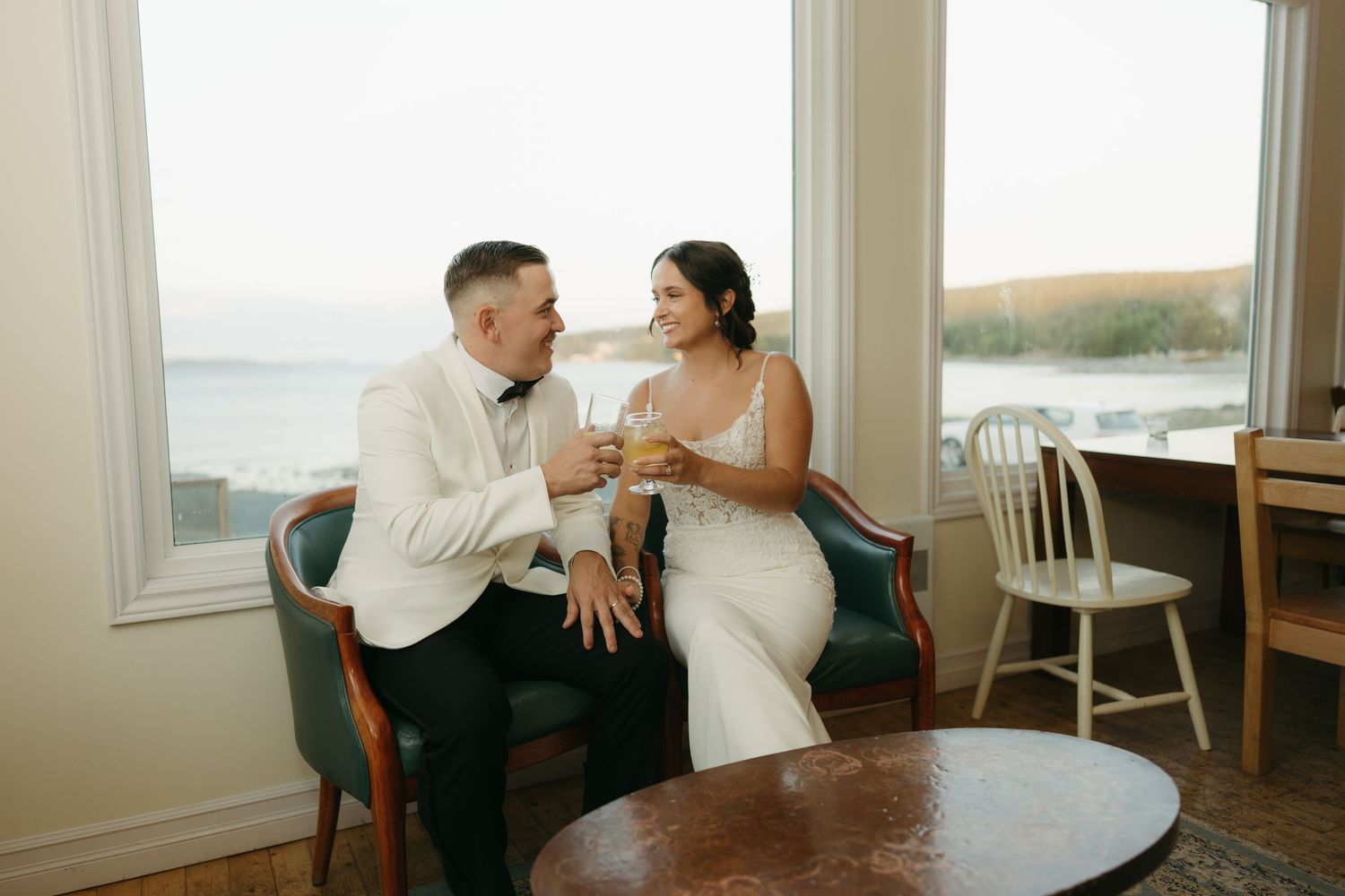 A couple shares a tender moment in a bright, sunlit room with white walls and window views.