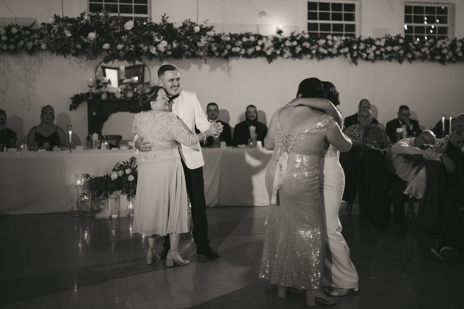 Wedding guests dancing together at a reception in a large hall with festive lighting and decor.
