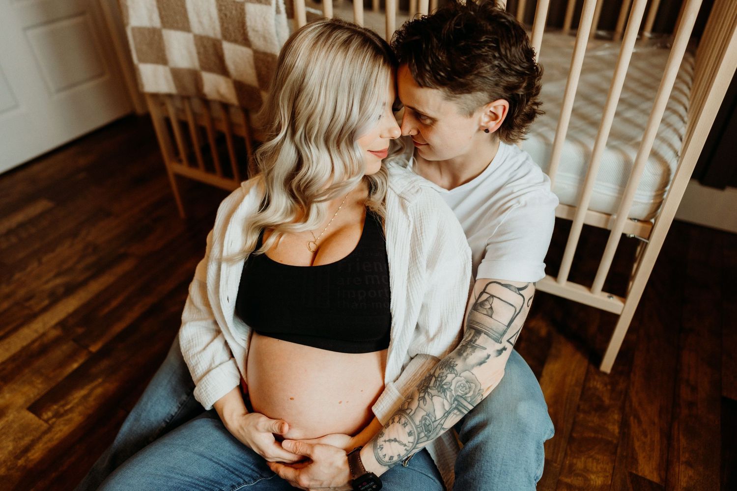 Intimate lifestyle maternity photos on wooden floor with natural window light.