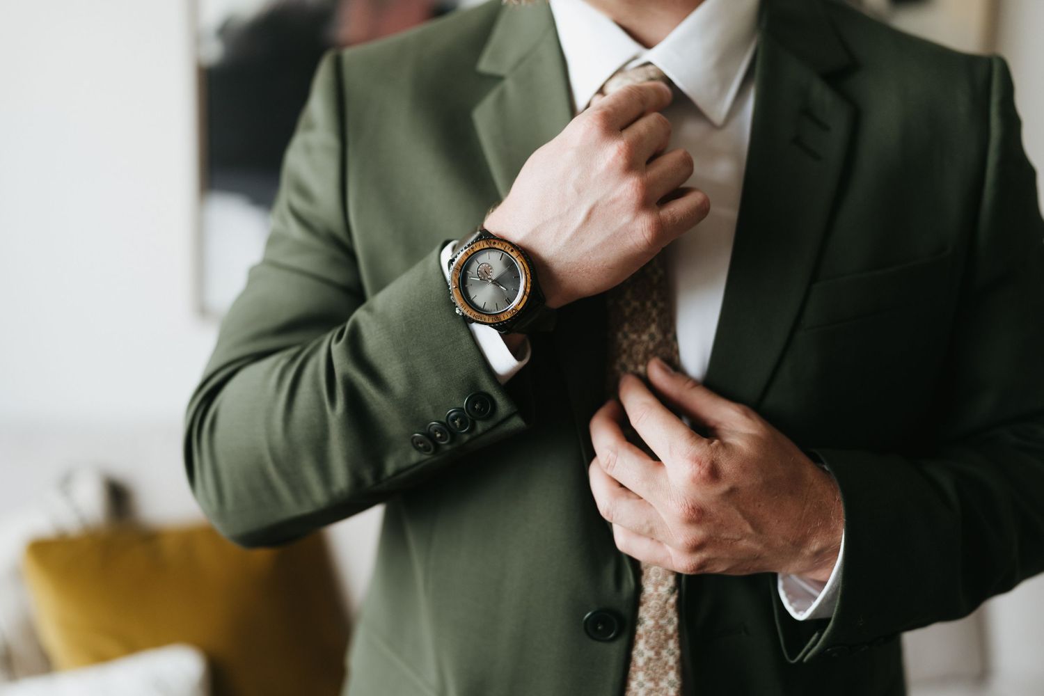 Man in olive green suit making final adjustments to formal attire.
