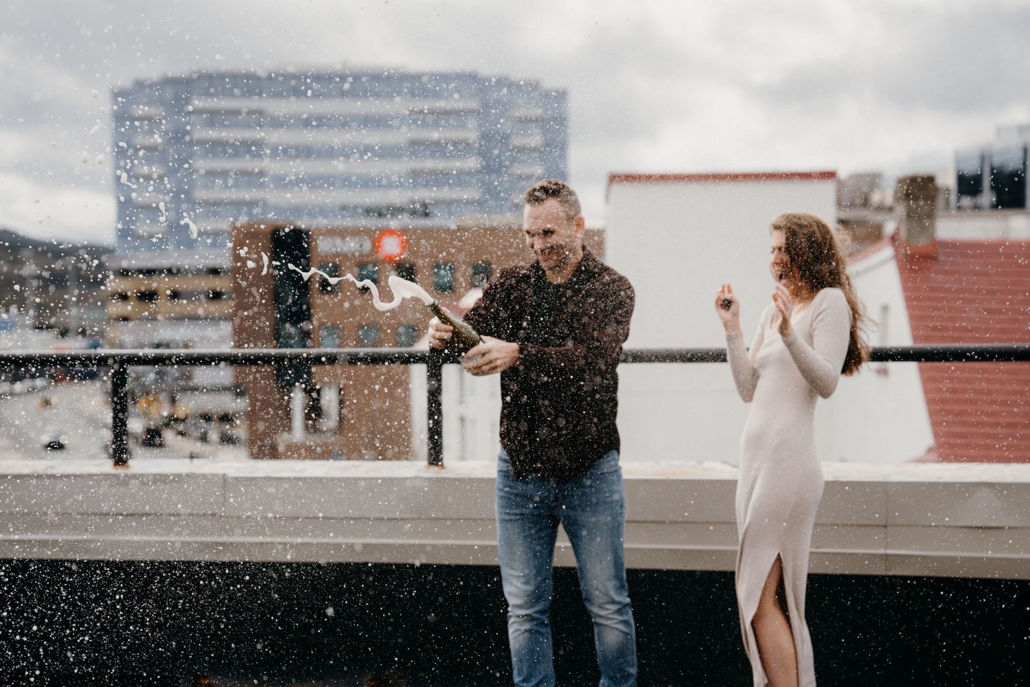 Two people share an intimate moment on an urban rooftop with tall buildings in the background.