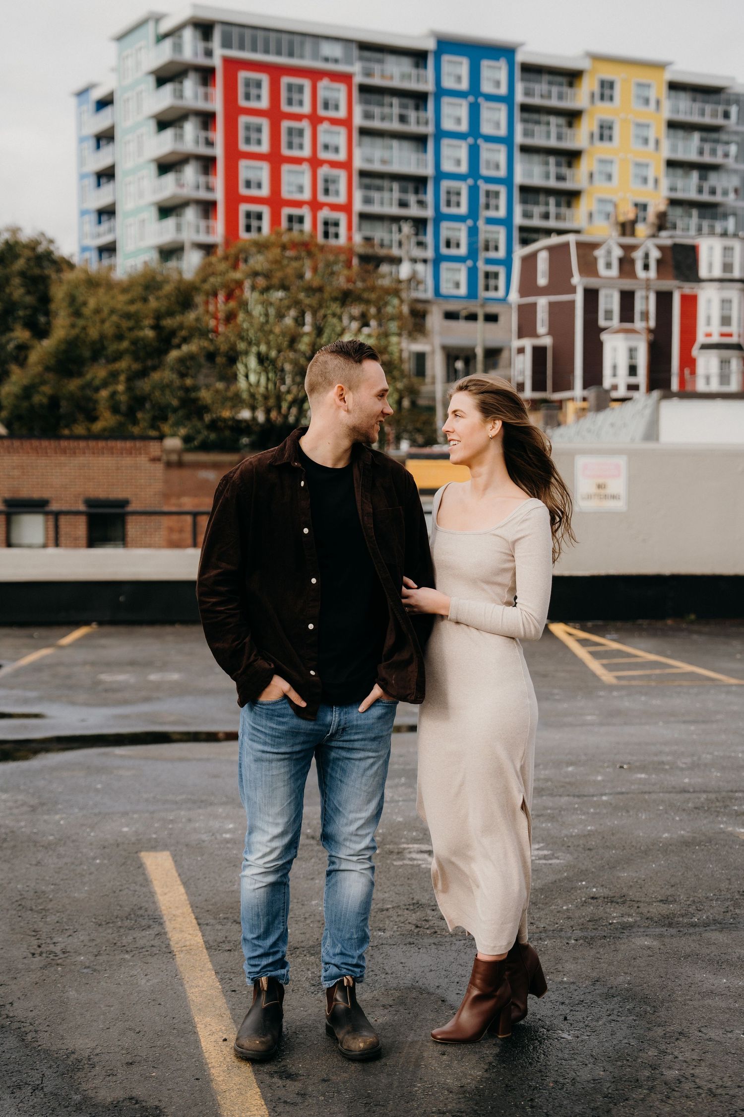 A sweet couple stops for a candid moment against an urban backdrop with vibrant buildings.