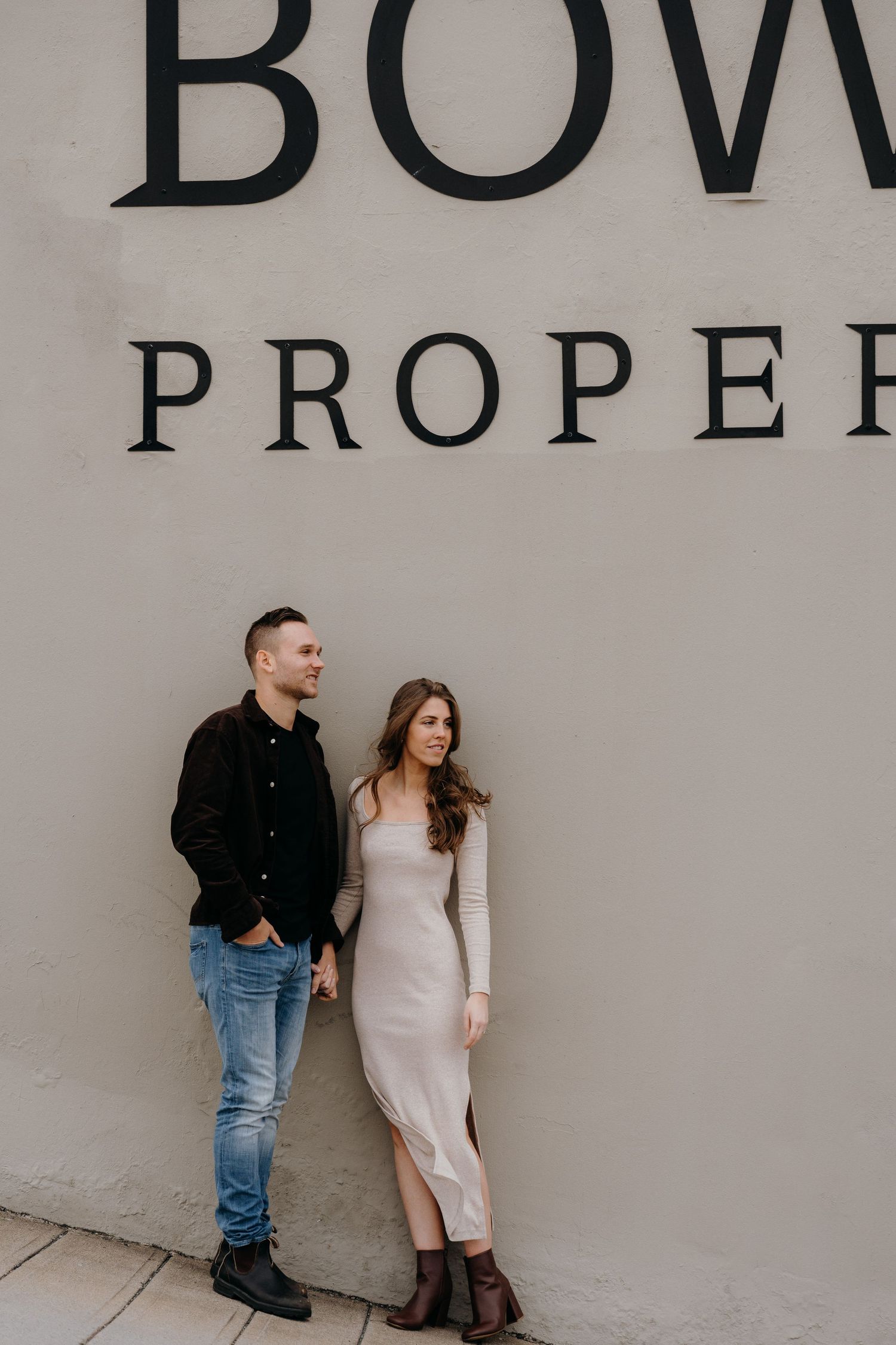A couple posing against a gray wall with Bowring Properties signage in an urban setting.