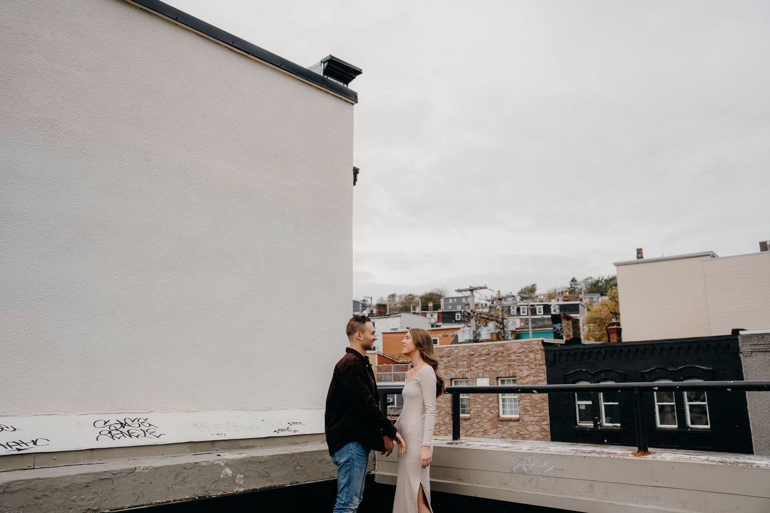 A rooftop view of an urban neighborhood with brick buildings and white walls against an overcast sky.