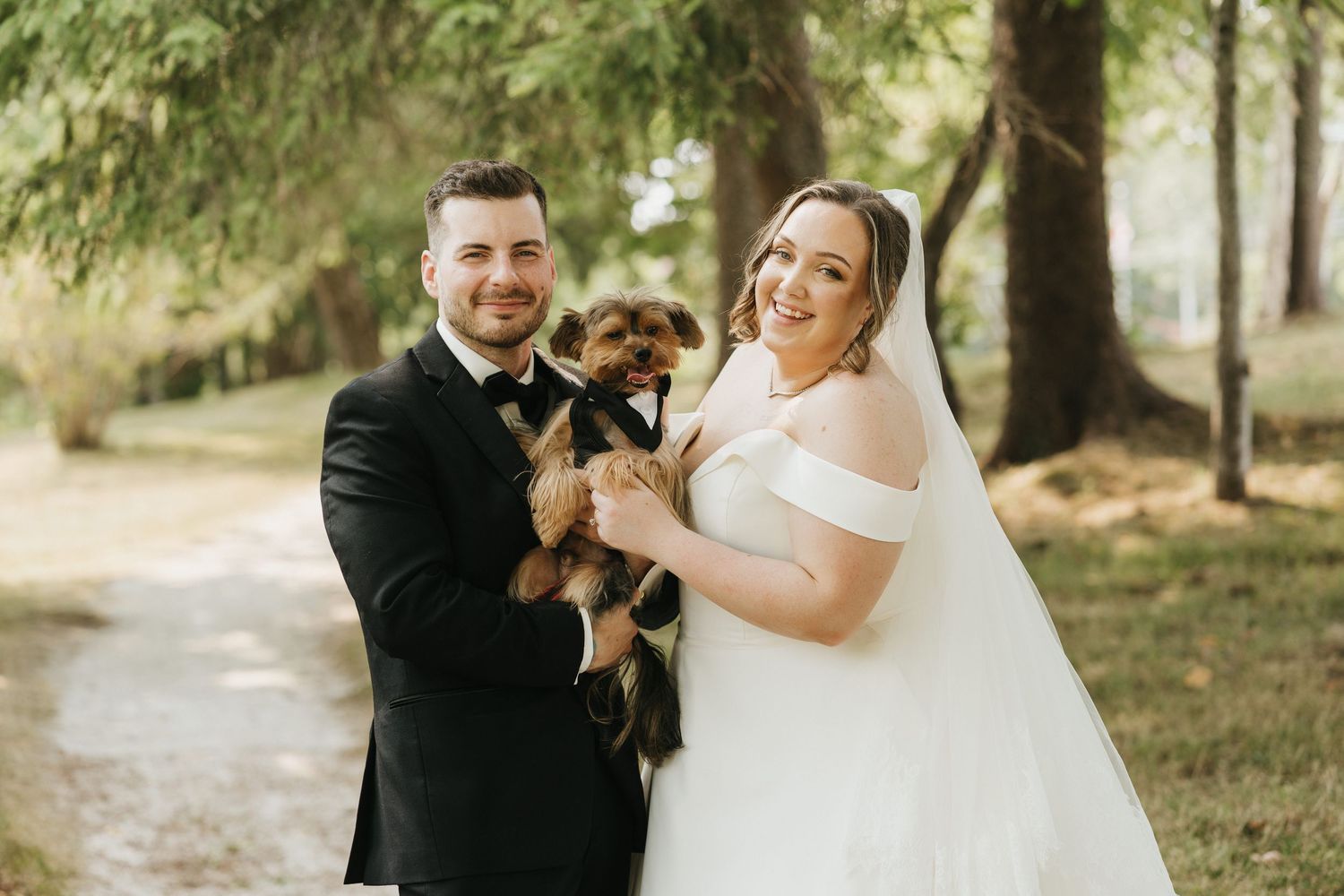 Bride and groom share candid moments with their pet dog during outdoor wedding photos.
