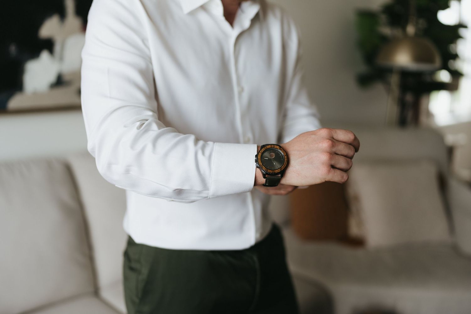 A figure wearing a crisp white shirt adjusts their sleeves in a minimalist indoor space.