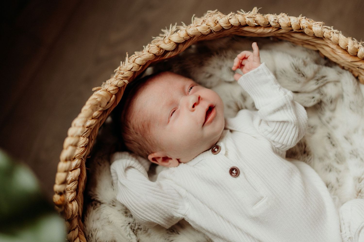 Newborn sleeping peacefully in a round woven basket wrapped in white fabric.