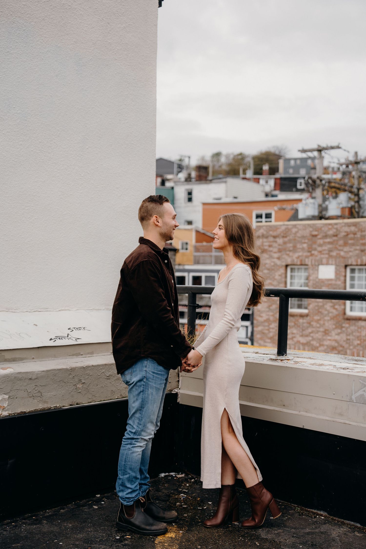 A couple shares a tender moment on a city rooftop with urban buildings in the background.