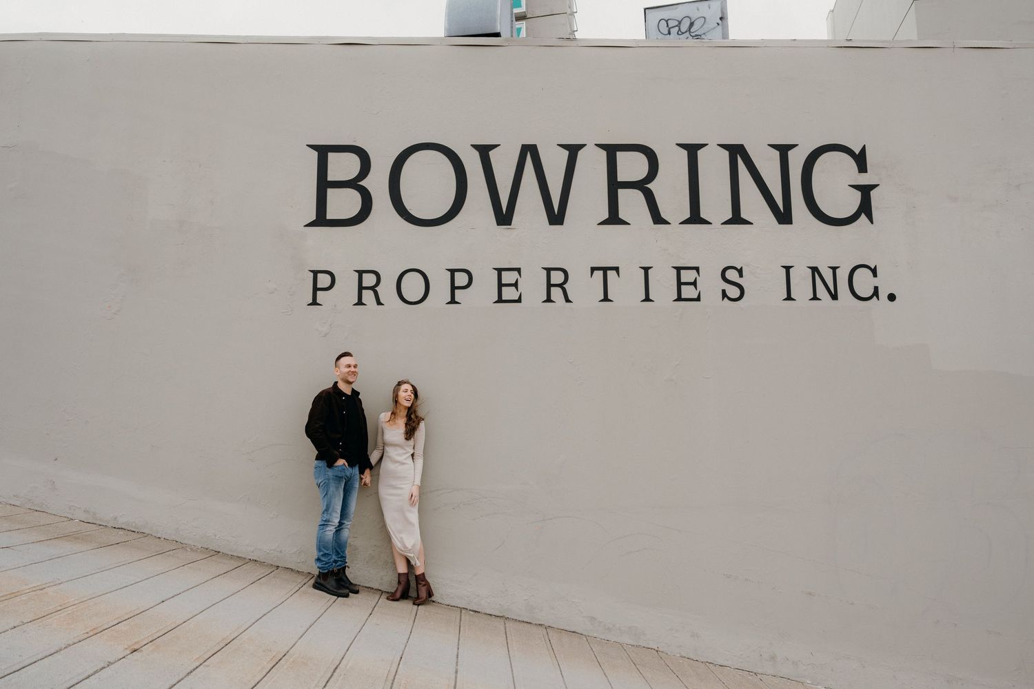 A couple standing together against a modern building wall with Bowring Properties text.