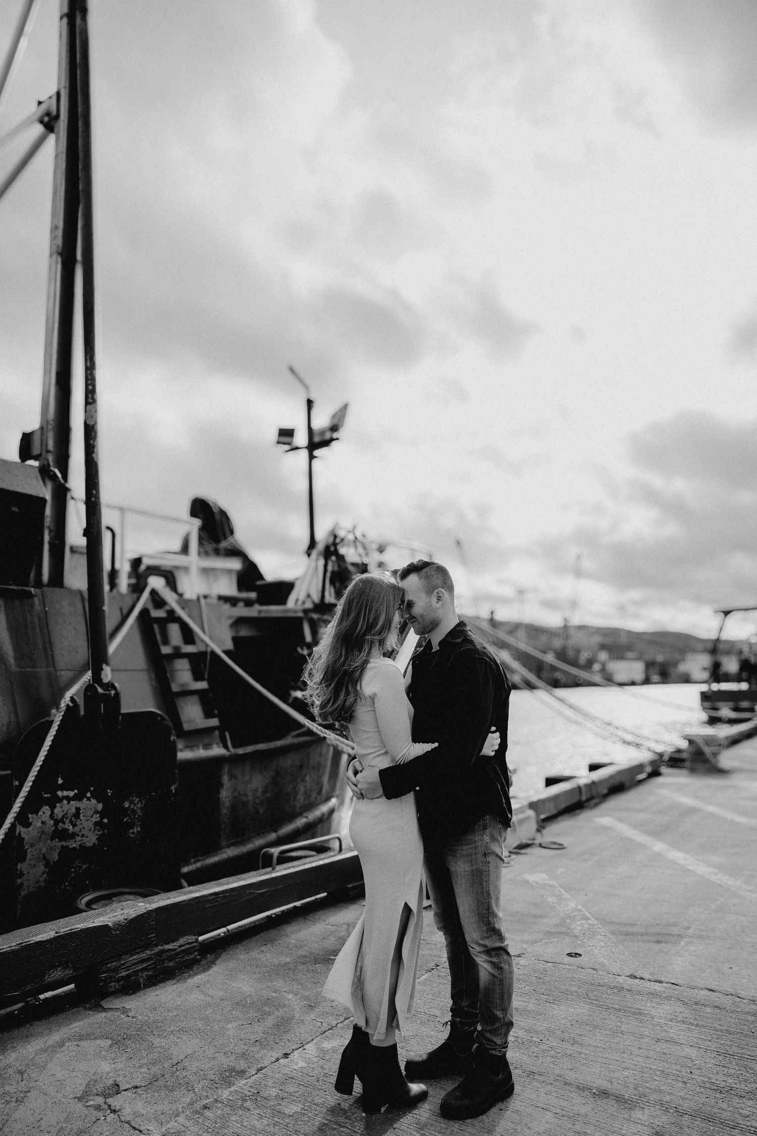 Black and white photograph of a couple sharing a moment on a harbor dock.