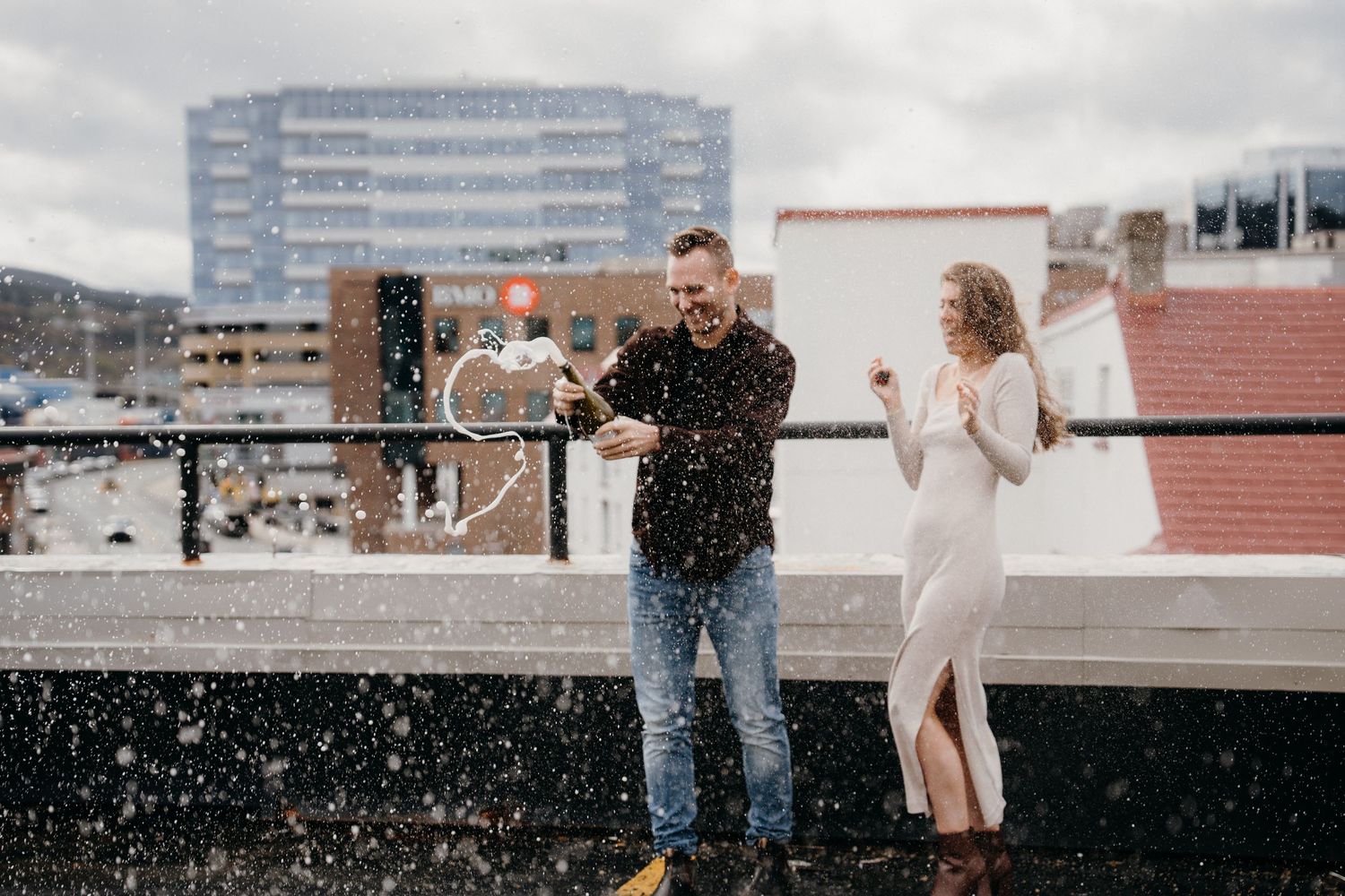 A couple celebrates a special moment on an urban rooftop terrace with city buildings visible behind them.