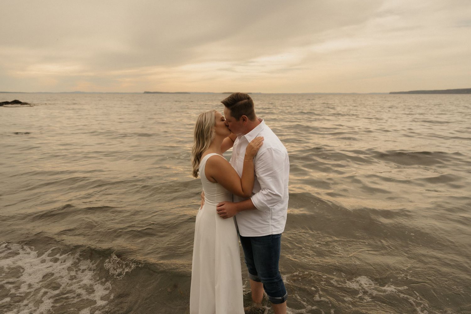 A couple shares romantic moments on a beach at sunset, embracing near the ocean's edge.