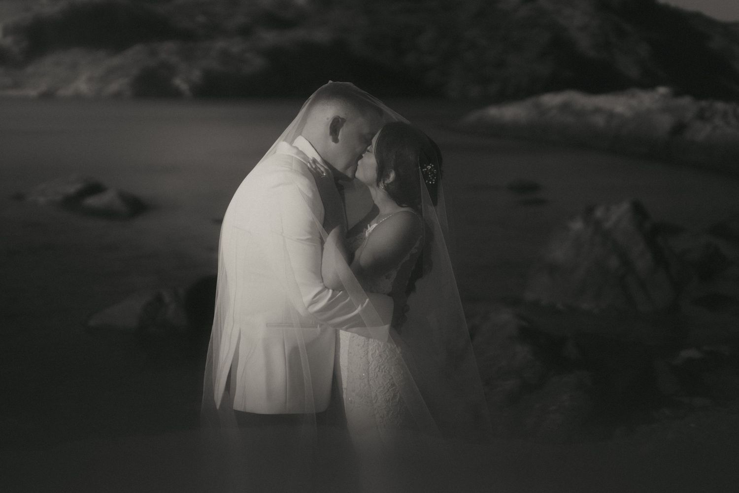 A romantic black and white wedding photo shows a couple embracing by a misty lake with mountains in the background.