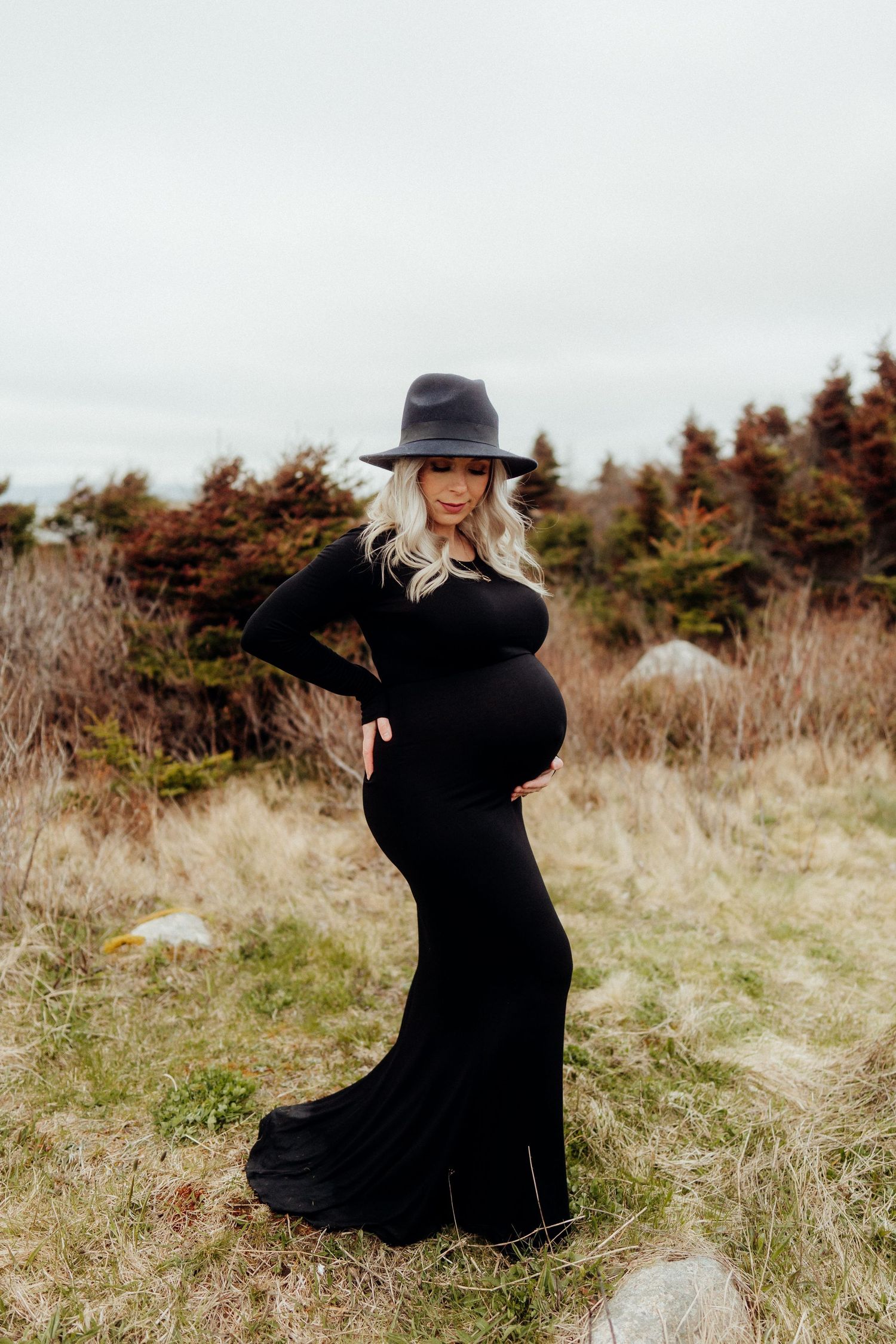 A person in black dress and hat poses dramatically in a field.