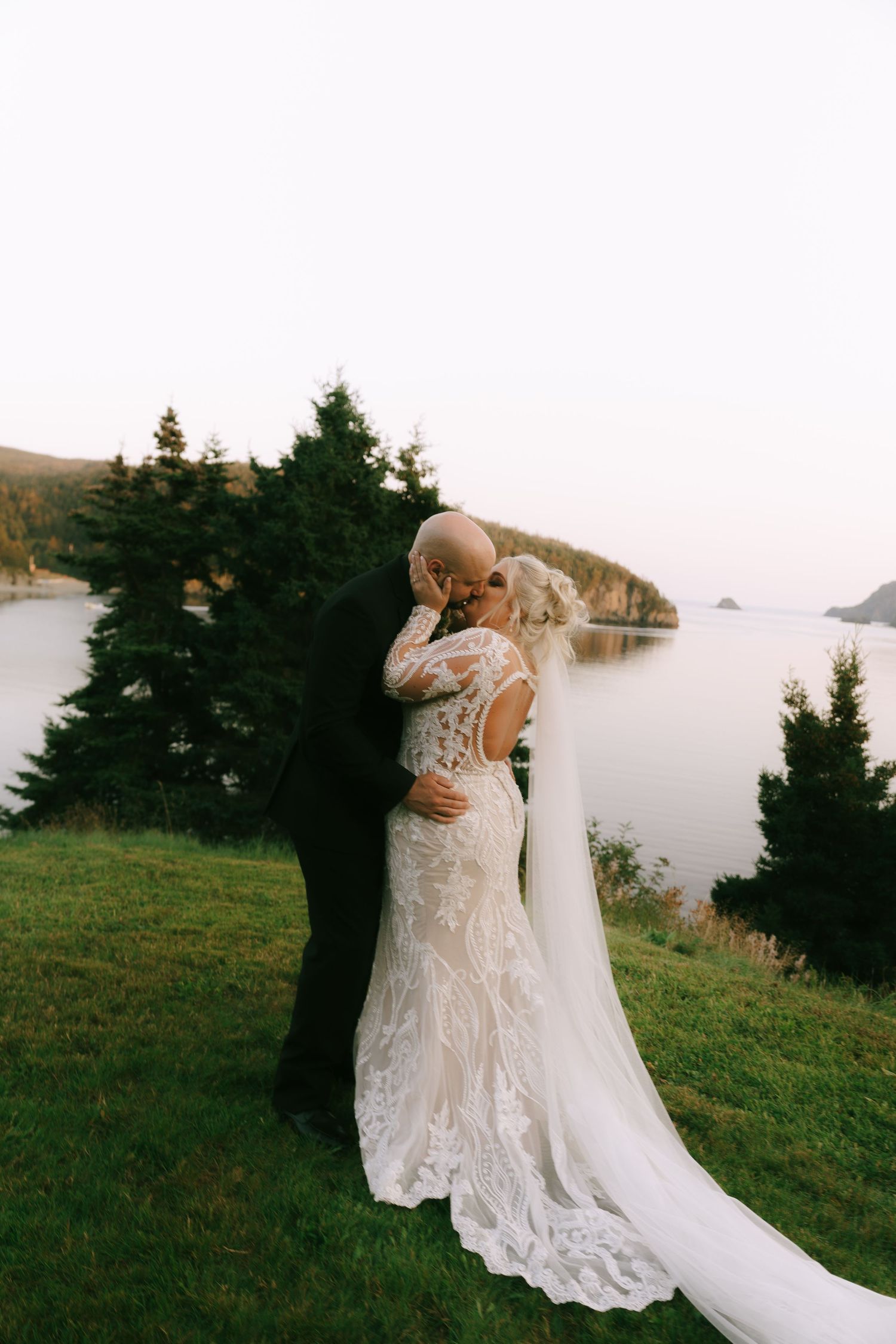 A couple shares an intimate moment on a coastal clifftop with ocean views at sunset.