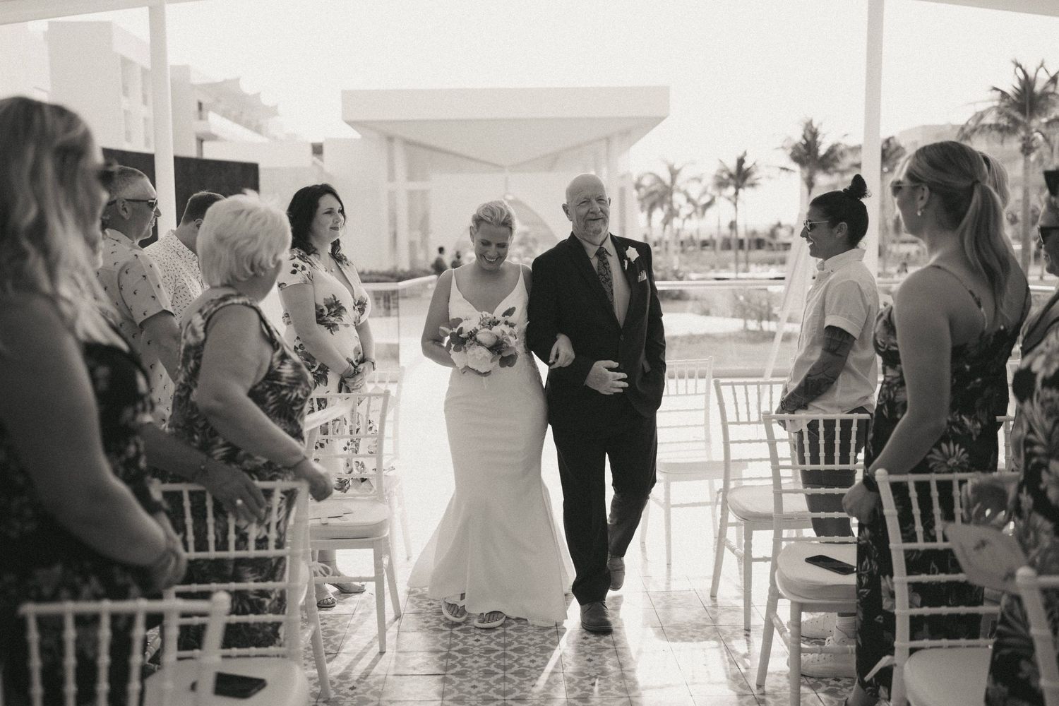 Wedding ceremony setup with white chairs and tropical palm trees in the background.