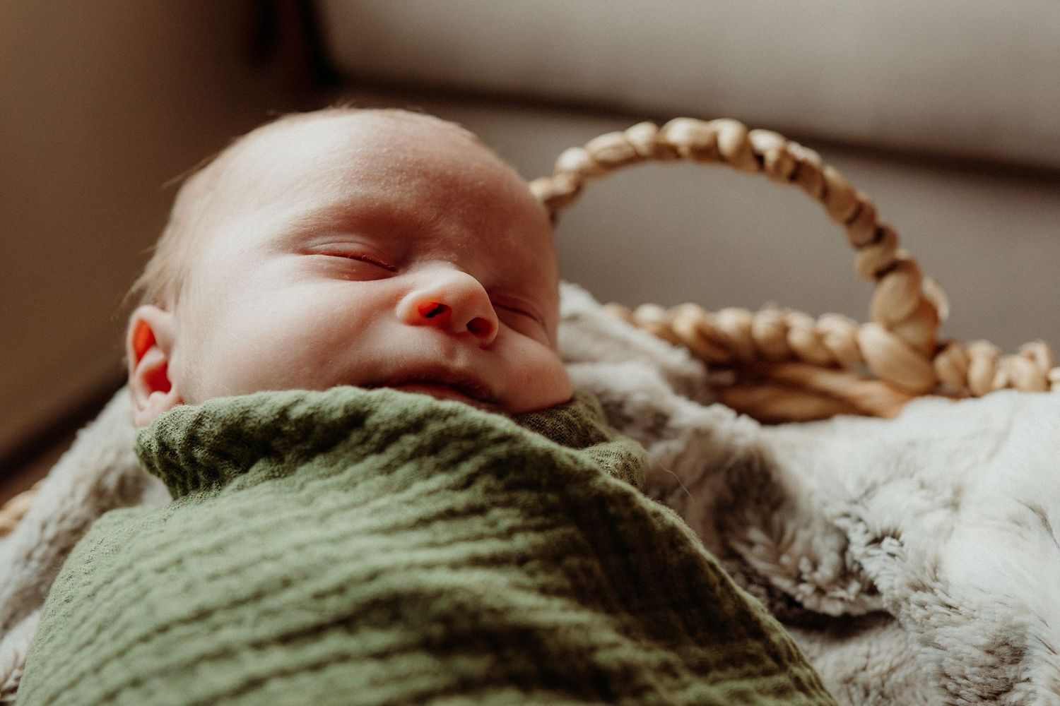 Close-up of sleeping baby in green wrap against white textured background.